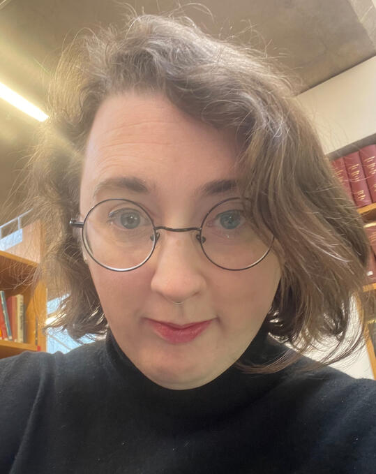 A profile of Maria. She has short brown hair and round glasses